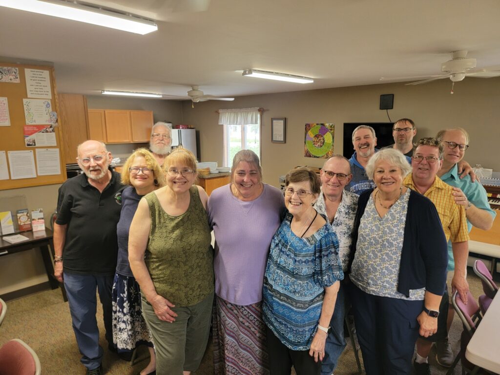 A group of adults gather together in a church hall and smile up at the camera. They're close together in the photo and the energy in the image communicates that they're relationally close, too.