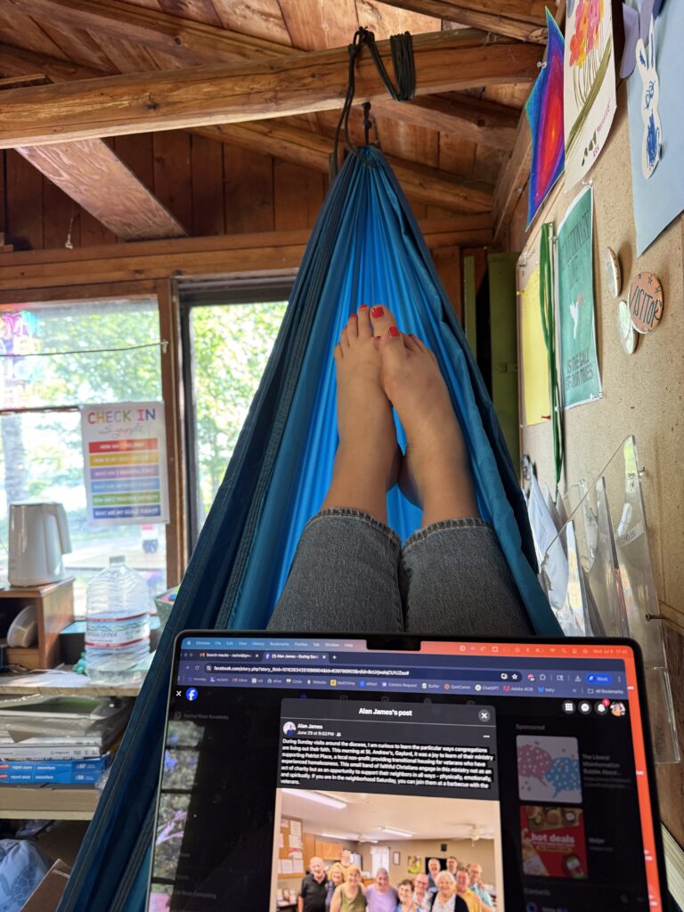 A photo of Rachel Rose-Ravellette holding her laptop in a hammock in the Director's office as she works from Camp Chickagami.