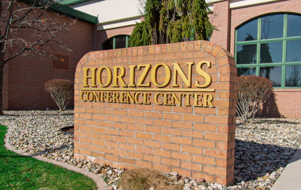 Image Description: A photo of the brick sign outside of the convention location which reads "Horizons Conference Center." The photo was taken on a bright sunny day.