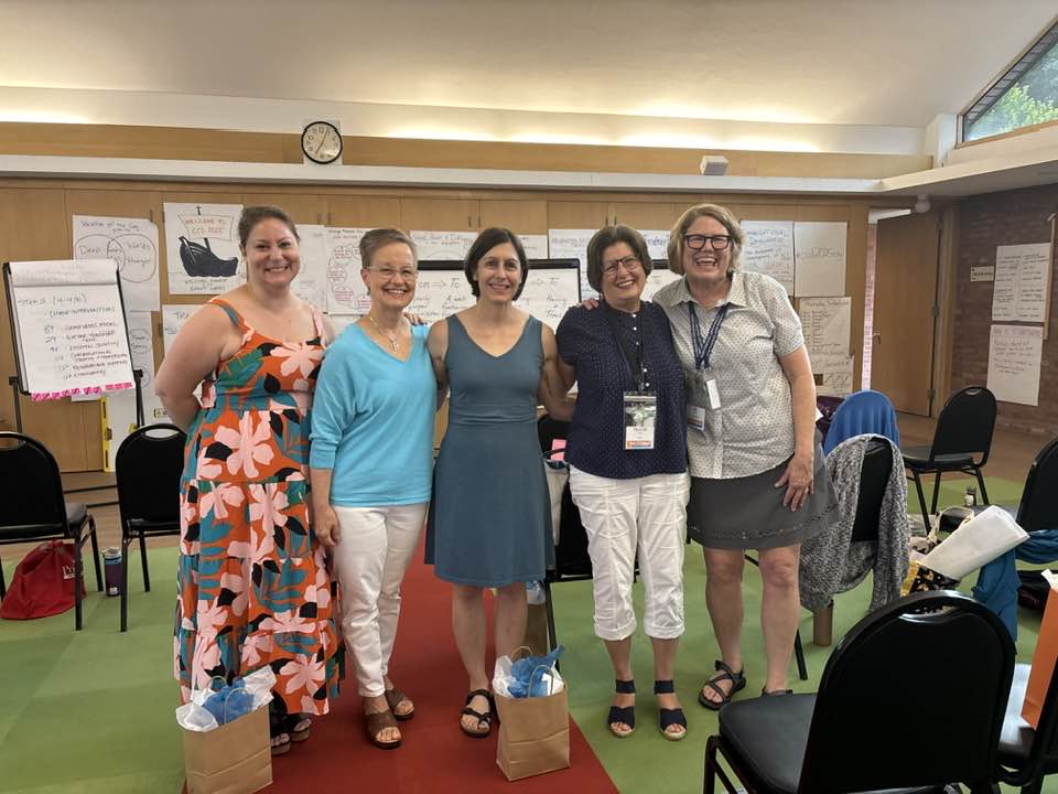 Image Description: A group of five priests and trainers for the College for Congregational Development smiles together in the parish hall at St. John's Episcopal Church in Midland. Behind them, the walls are covered with large format post-it notes full of models and other drawings and text, the signature presentation mode for CCD curriculum. From left to right, the first three women are the guest trainers, Martha, Katrina, and Kate. Then is our own Canon Tracie Little and Mtr. BJ Heyboer.