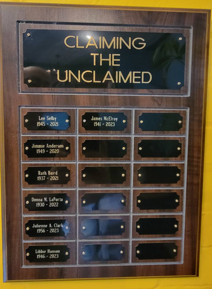 Image Description: A detail shot of a plaque at Epiphany South Haven. The top of the plaque reads "Claiming the Unclaimed," which is the name of the ministry of Epiphany wherein they take the unclaimed cremains from local mortuaries and give the individuals a respectful burial in the parish's memorial garden. The names of claimed individuals and their dates of birth and death (when known) fill the rest of the plaque.