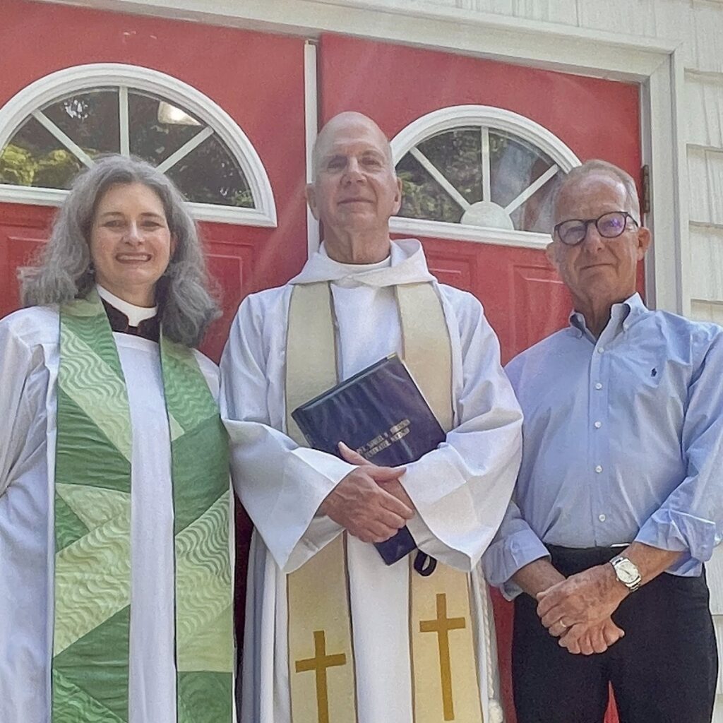 IMAGE DESCRIPTION: Two priests and another gentleman stand in front of St. James in Pentwater.
