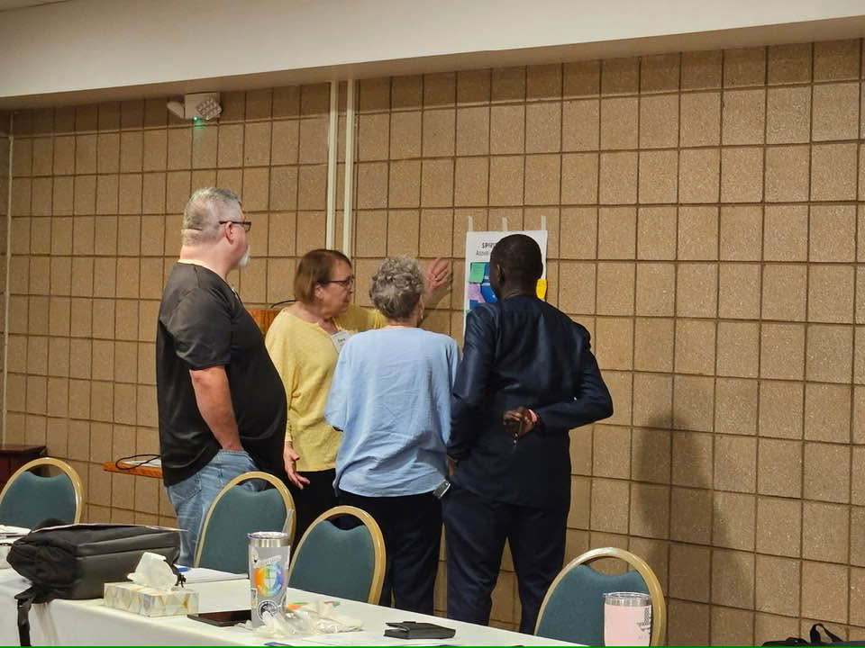 IMAGE DESCRIPTION: A group of people talk together by a poster on a wall. It seems like they're working together on a group activity.