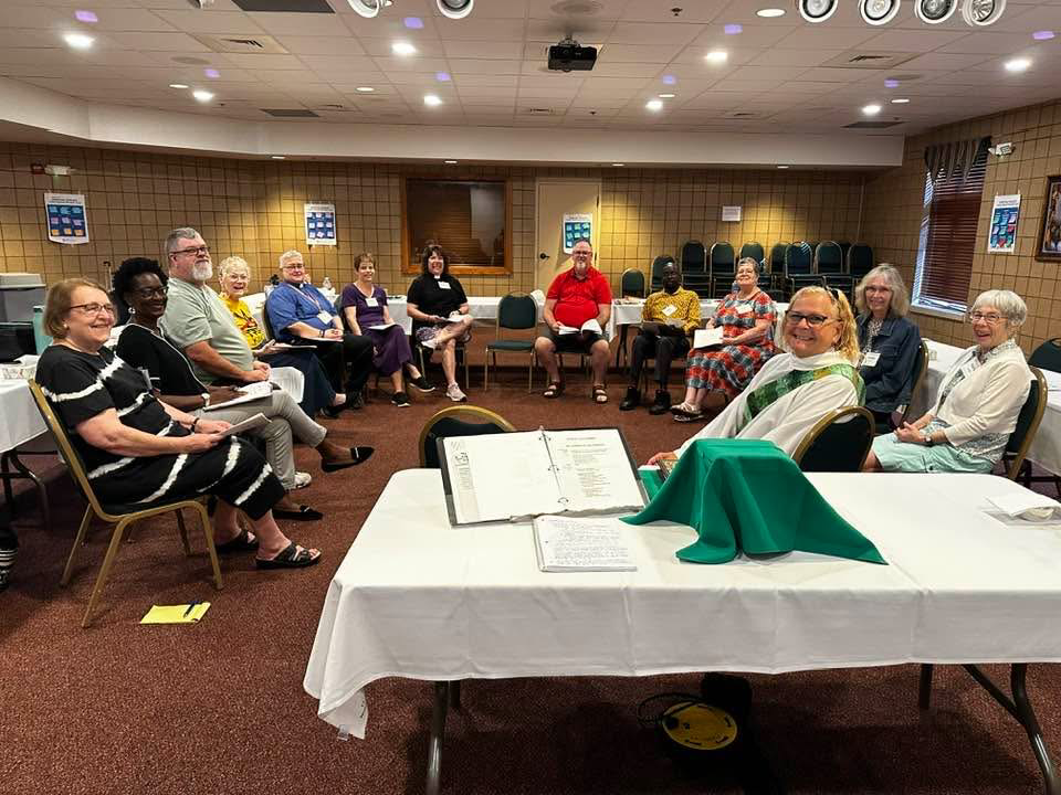 IMAGE DESCRIPTION: A group of people are sitting in a circle, but they're all turned to face the camera. An altar is set on a table in the foreground.