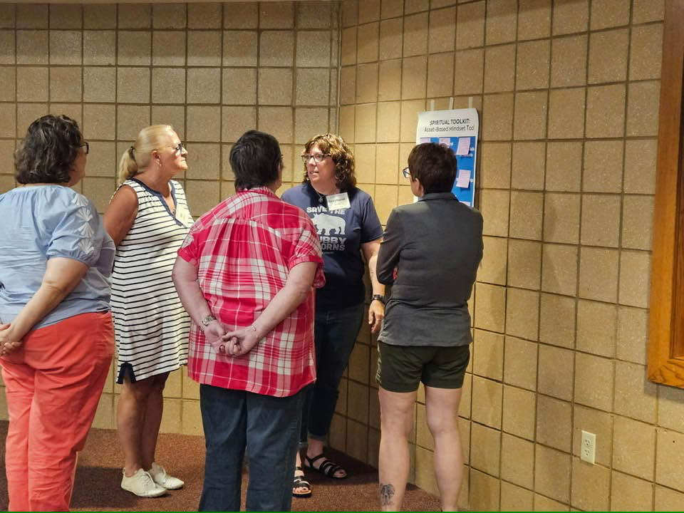 IMAGE DESCRIPTION: A group of people talk together by a poster on a wall. It seems like they're working together on a group activity.