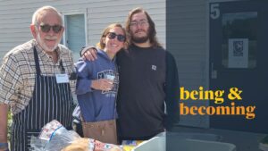 Three people stand smiling in front of a beige building. The man on the left wears sunglasses and an apron, the woman in the middle holds a drink, and the man on the right has his arm around her. Text reads being & becoming.