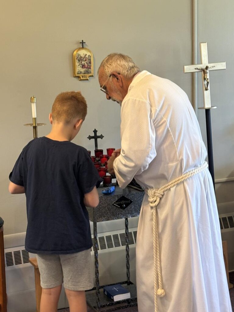 IMAGE DESCRIPTION: An older acolyte and his grandson work together to light candles at a prayer altar.