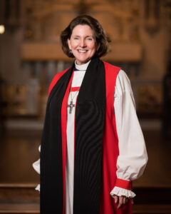 A formal portrait of the Rt. Rev. Anne E. Hodges-Copple. She smiles toward the camera and is vested in the traditional episcopal rochet and chimere.