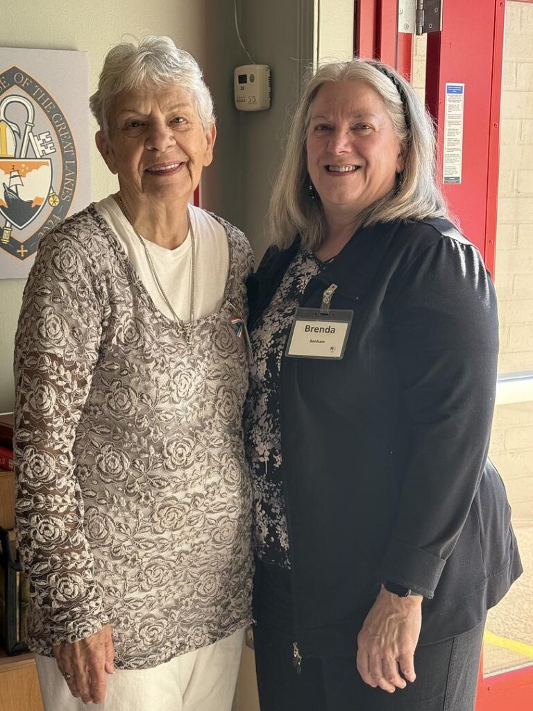 IMAGE DESCRIPTION: Two women stand together in front of the open red door at Holy Spirit Belmont.
