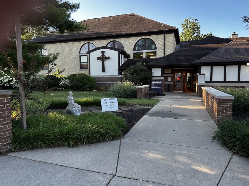 Exterior of St. John's Episcopal Church in Sturgis. A statue of St. Francis is visible, along with a large celtic cross on the side of the building.