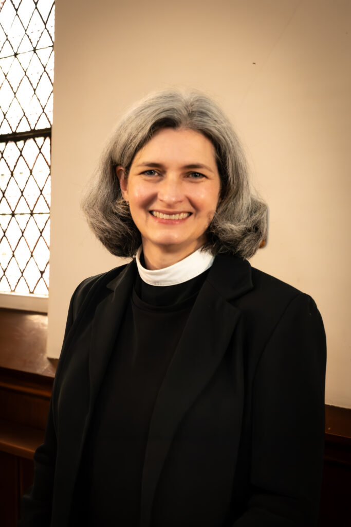 A headshot of Nurya Love Parish. She has grey hair and is wearing clericals and a black jacket.