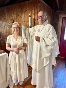 Image description: Kayleigh Gregg, wearing a white dress, stands next to Fr. Mike Fedewa. He is placing one hand on her head.